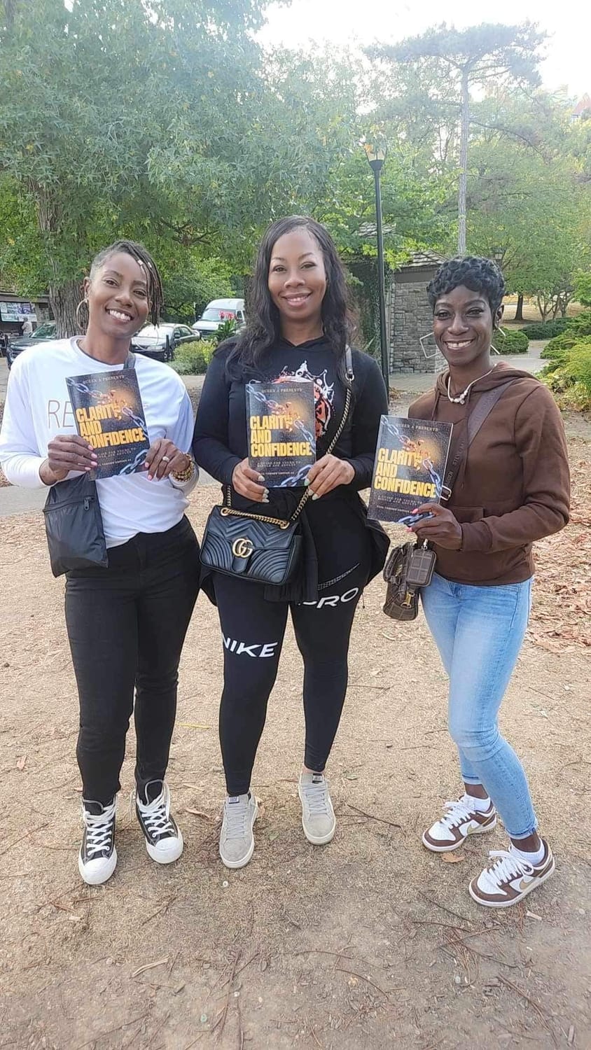 Three people holding copies of Clarity and Confidence outdoors