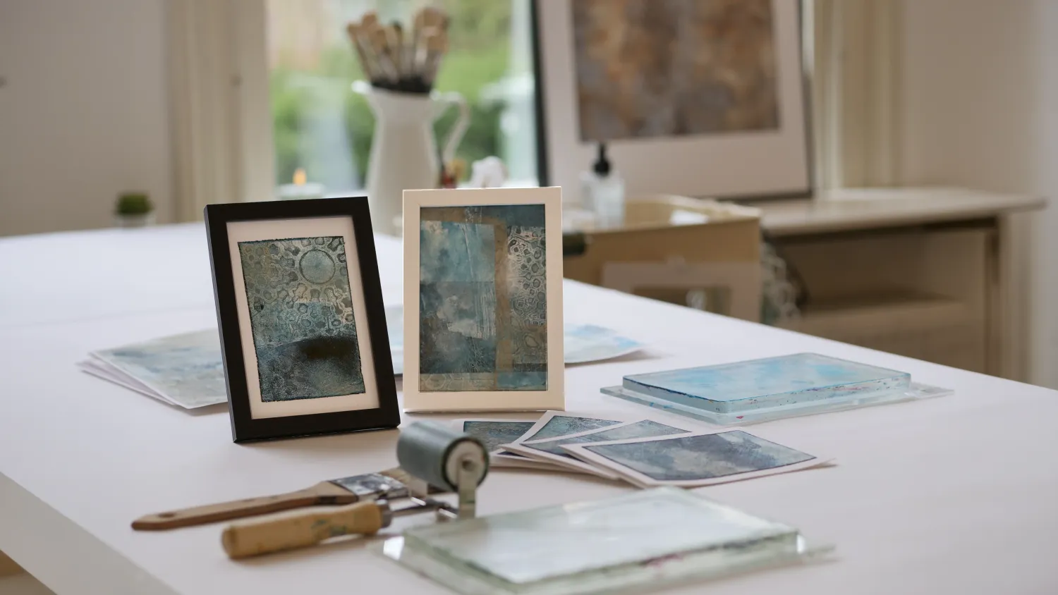 Ingelijste monoprints op de werktafel in het atelier
