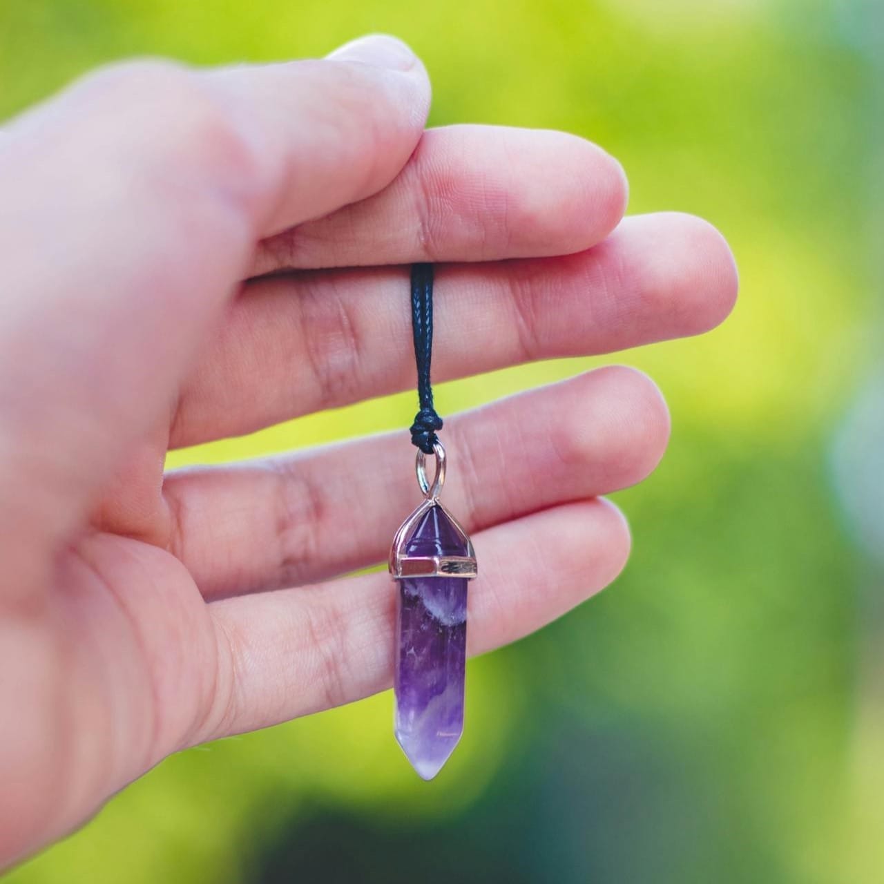 Ένα χέρι κρατά ένα εκρεμμές από αμέθυστο