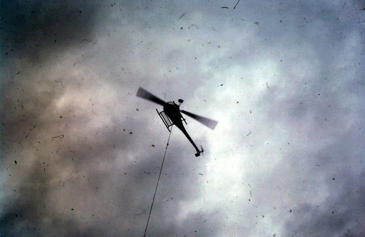 A silhouette of Eric Pittman’s helicopter performing a 200-foot longline lift over a cliffside forest, demonstrating the machine's technical capability