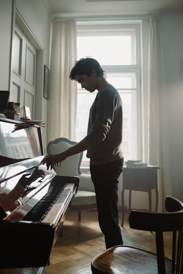 Teen boy standing at the piano.  Sounds of Joy Music Studio.