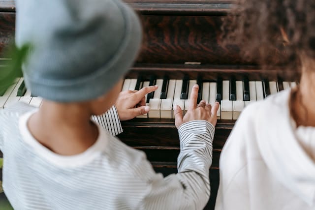Young boy practicing piano with his big sister.  Sounds of Joy Music Studio.