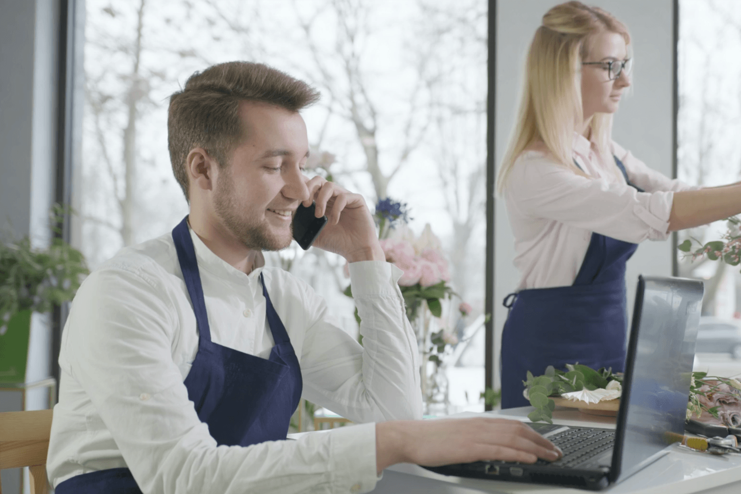 Freundliche Blumenladen-Inhaberin arbeitet an ihrem Laptop zwischen bunten Blumen in ihrem Geschäft