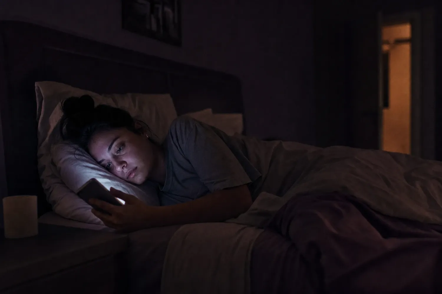 A woman lying in bed at night, her face lit only by her phone screen