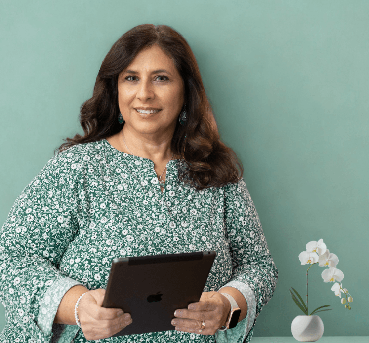Janet holding a tablet and smiling with a orchid on the desk behind hr