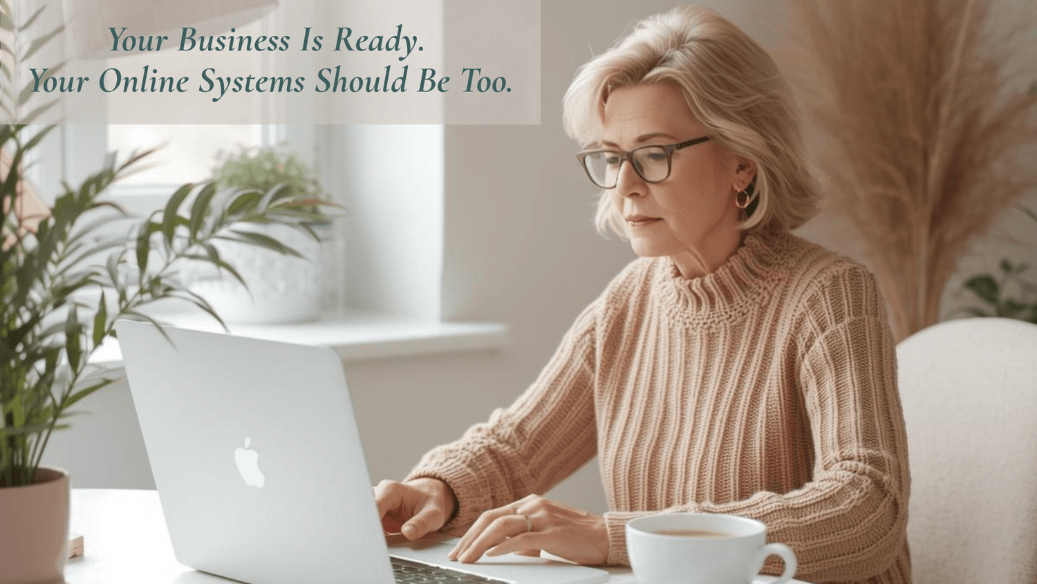 mature woman sitting at desk working on laptop with coffee beside her and plant next to laptop hero image for website