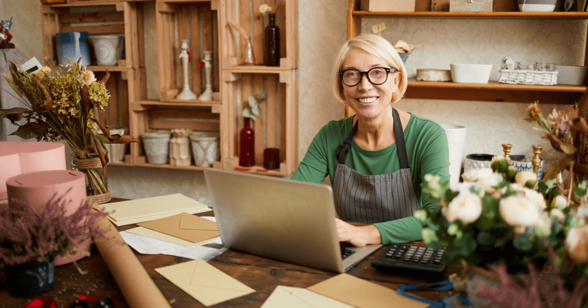 a smiling woman working at a laptop in a flower shop