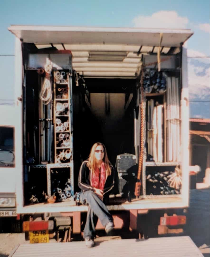 Photo de tournage avec France Dumas assise à l'arrière du camion des électriciens, les pieds sur la hayon au sol - tournage France 3 en 2024