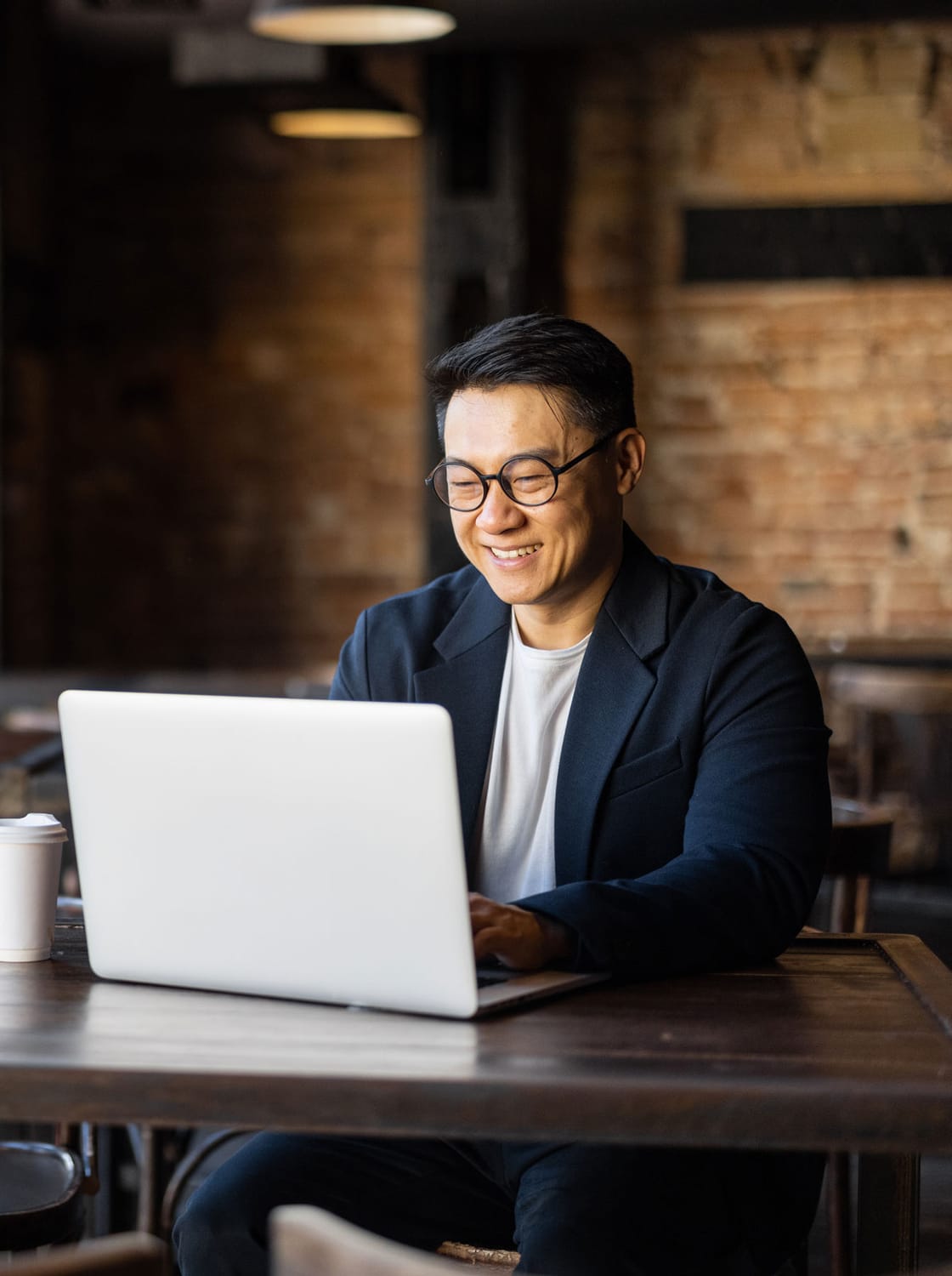 an asian man smiling while on his laptop in a coffee shop