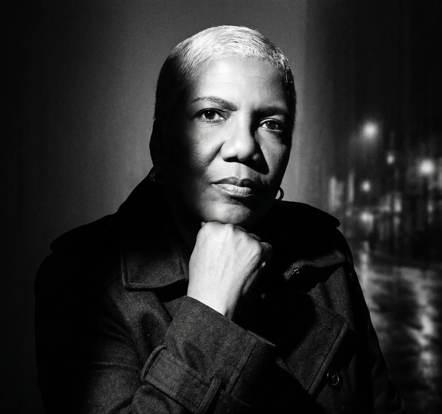 Portrait of Chrislyn Benjamin, founder of Fuel Soul Coach, wearing a dark trench coat with dramatic chiaroscuro lighting and a city street background.