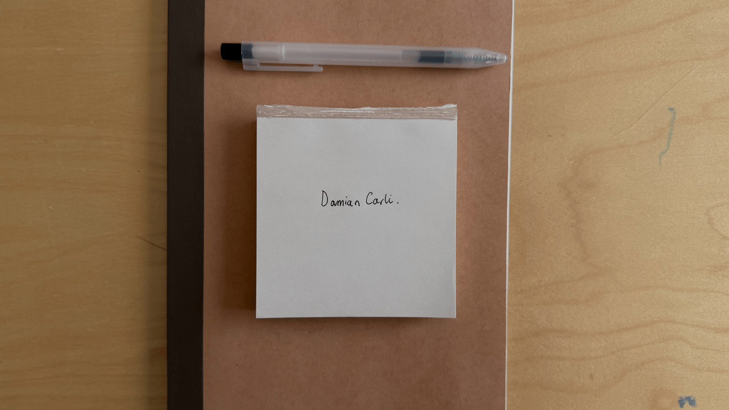 A name written on a plain paper pad on a wooden desk, with a pen beside it.