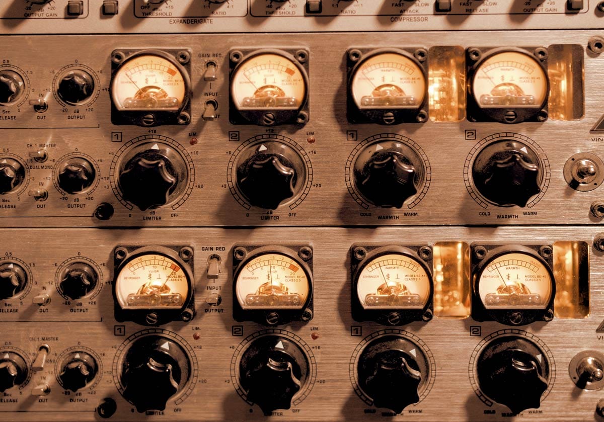 Close-up view of a vintage dual-channel analog outboard processor showing detailed VU meters, large black control knobs, and illuminated warm orange status lights on a brushed metal faceplate.