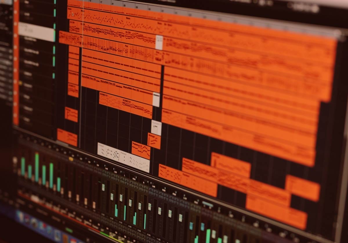 A digital audio workstation interface showing multiple tracks arranged on a timeline above a mixing console with faders and meters.”