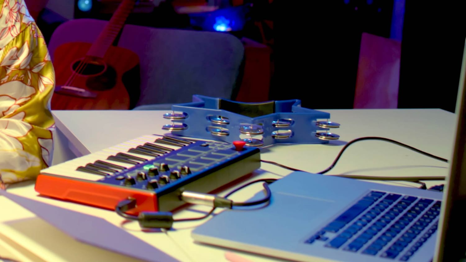A tabletop music setup with a small MIDI keyboard, laptop, tambourine, and guitar, showing how simple tools can be used to start making music right away.