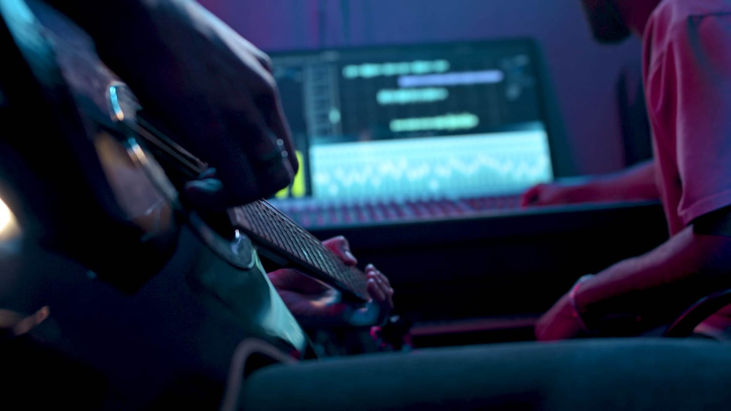 A close‑up of someone playing guitar while another person edits audio in a DAW, capturing the moment where musical ideas first come to life and showing how simple beginnings can lead to real music production.