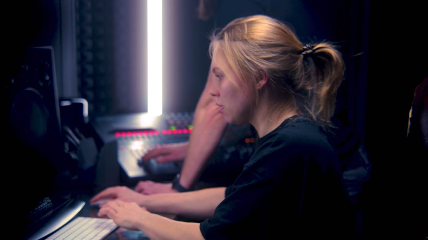 Two musicians working together in a studio, one editing on a computer and another adjusting a mixing console, representing creators who want more realistic and expressive MIDI performances.