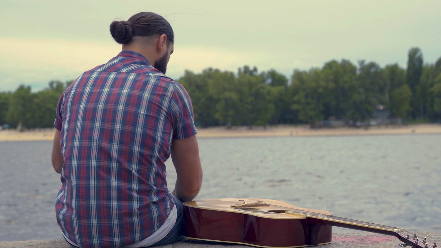 A sad songwriter sits next to a river, representing the frustration of failing to finish a song idea.