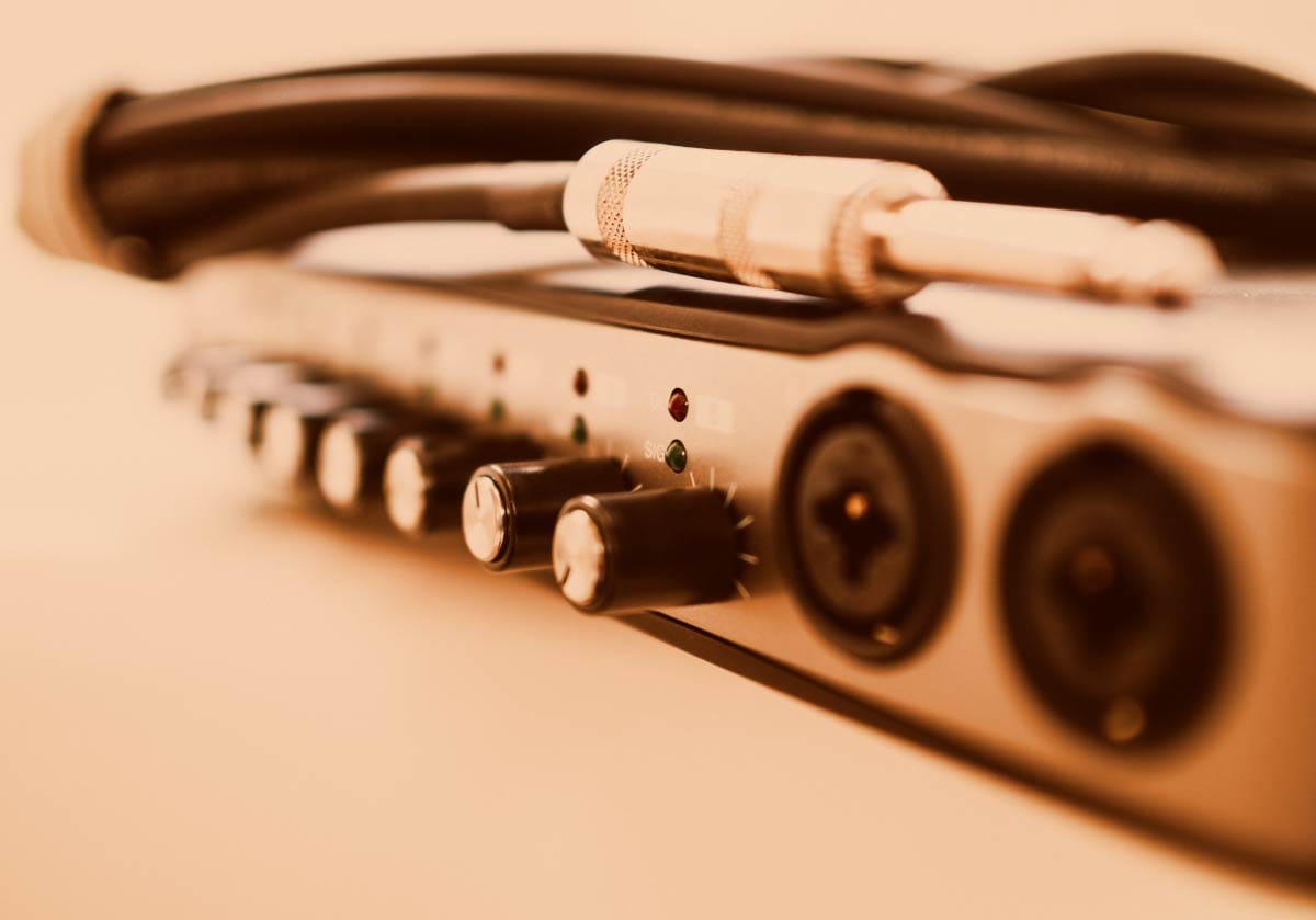 Close-up of an external USB audio interface with physical control knobs, XLR combo inputs, and a quarter-inch instrument patch cable resting on top in warm lighting. A hero image for a guide on audio interfaces.