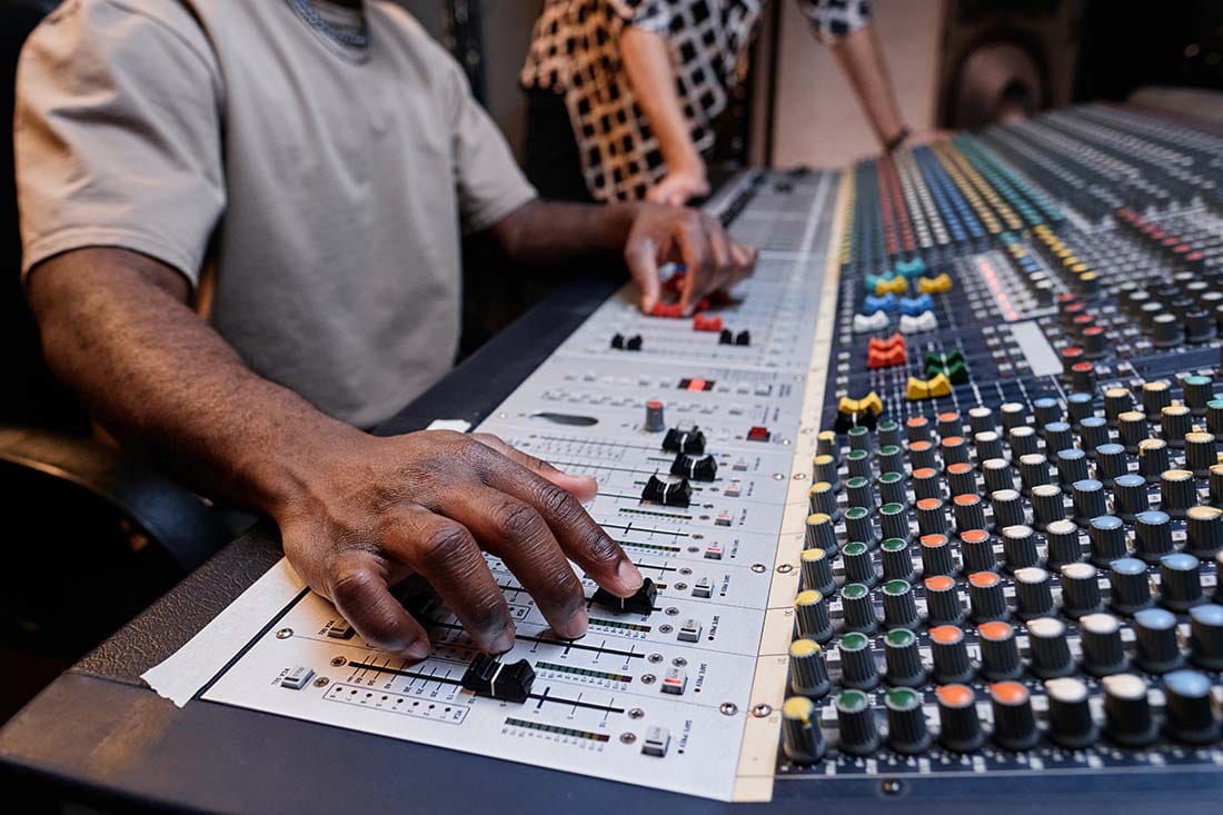 A close-up view of an audio engineer's hands adjusting channel faders and rotary knobs on a large-format professional analog mixing console.
