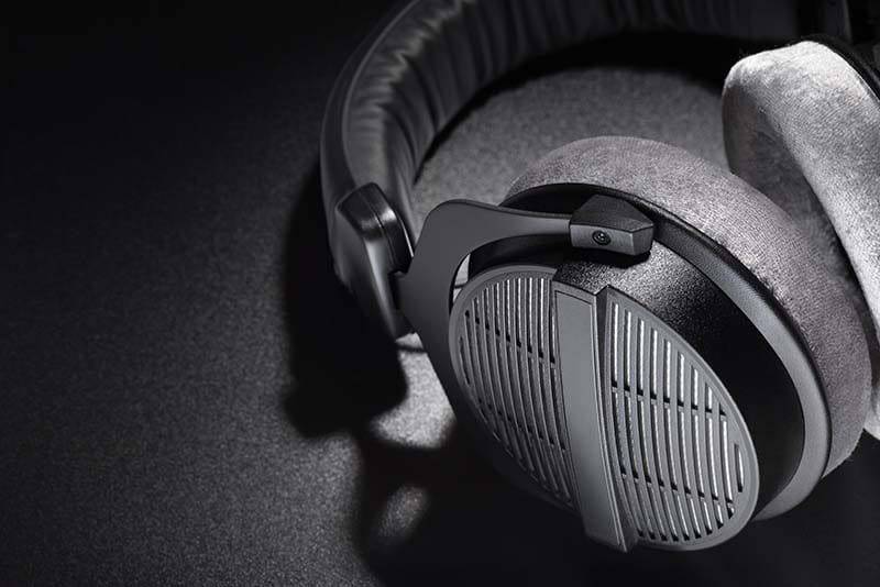 A detailed close-up shot of an open-back studio headphone cup showcasing its slotted metal grille design and plush grey velour ear pads.