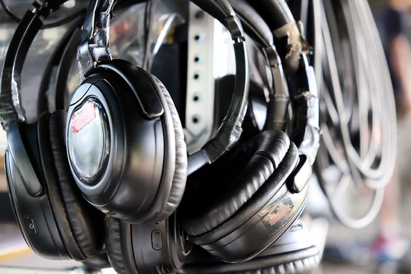 A close-up shot of multiple well-worn studio tracking headphones heavily reinforced with black electrical tape hanging from a storage rack in a recording environment.