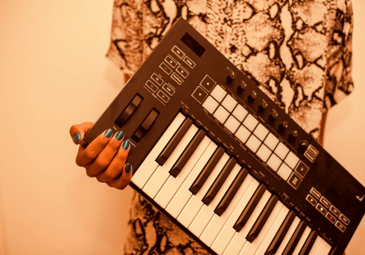 Music producer holding a compact 25-key USB MIDI controller keyboard with velocity-sensitive drum pads