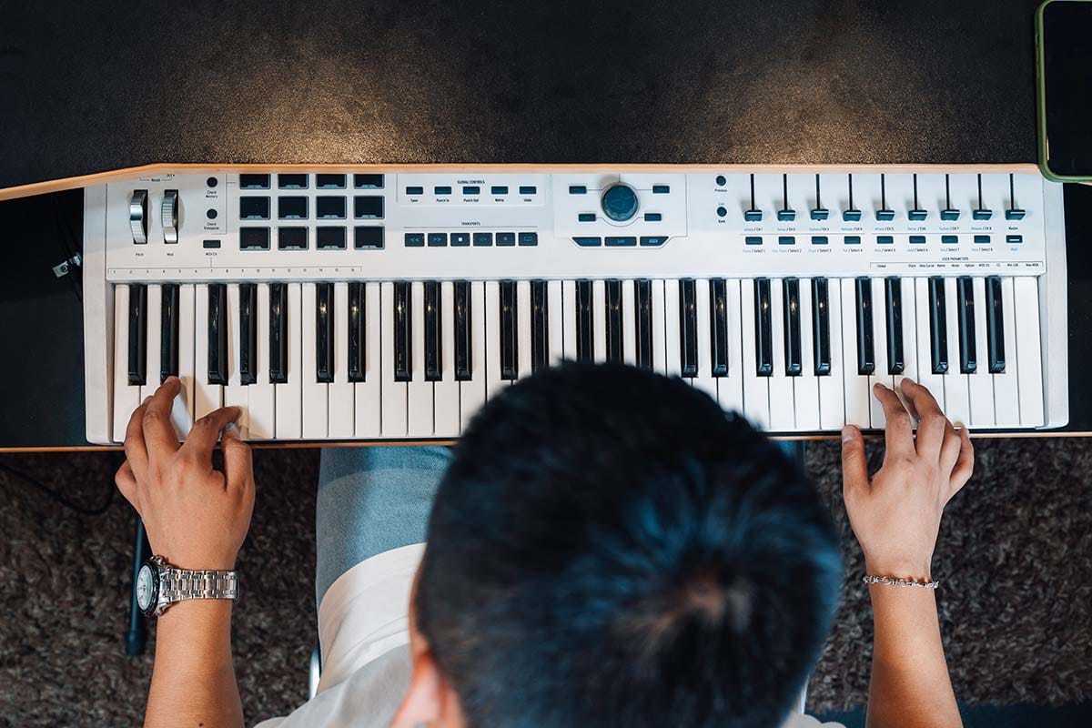 Top-down overhead view of a producer playing a 61-key MIDI keyboard controller at a studio desk