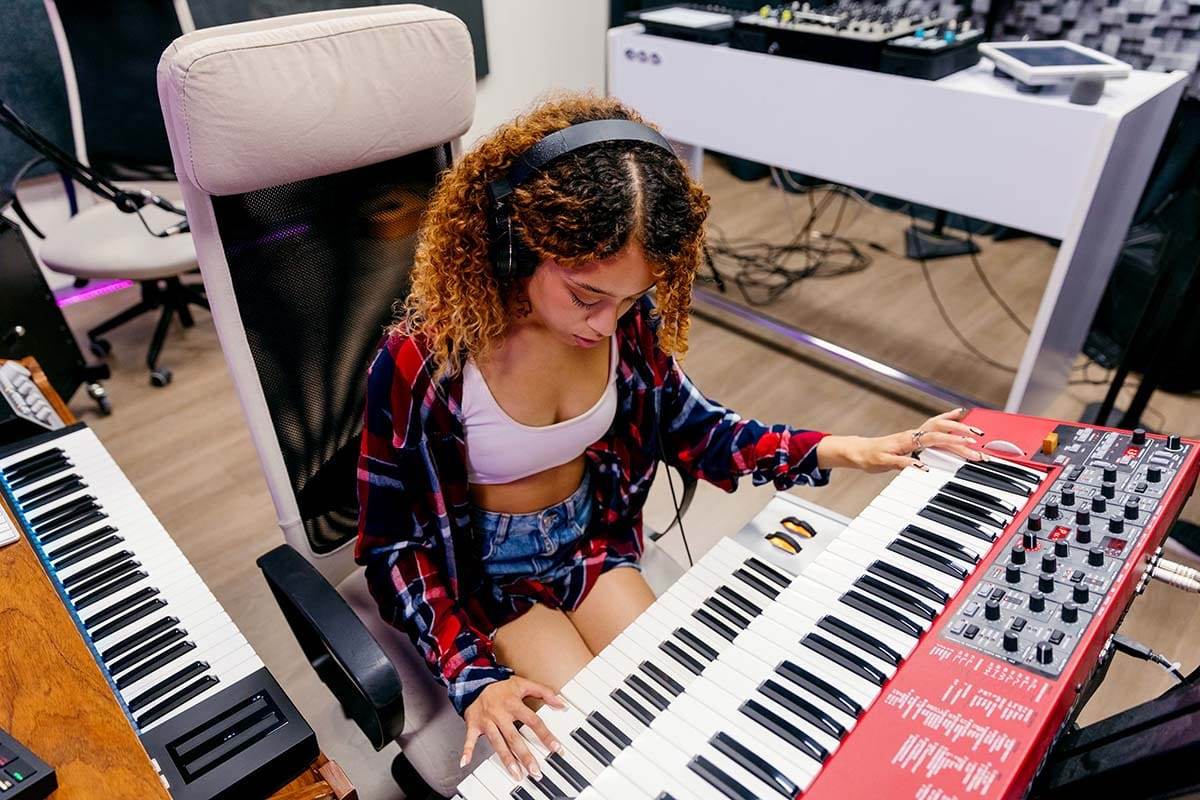 Producer wearing studio headphones while playing a hardware keyboard controller in a home recording setup
