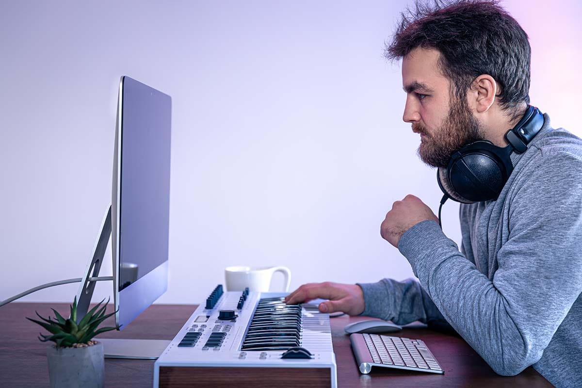 Music producer sitting at a computer desk wearing studio headphones while learning DAW software layout