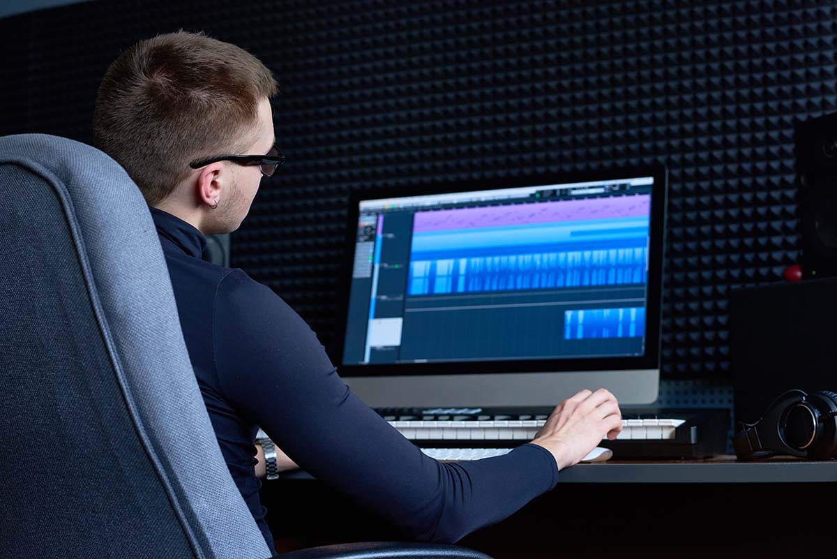 Music producer working in a DAW arrangement timeline view while monitoring audio latency and CPU load