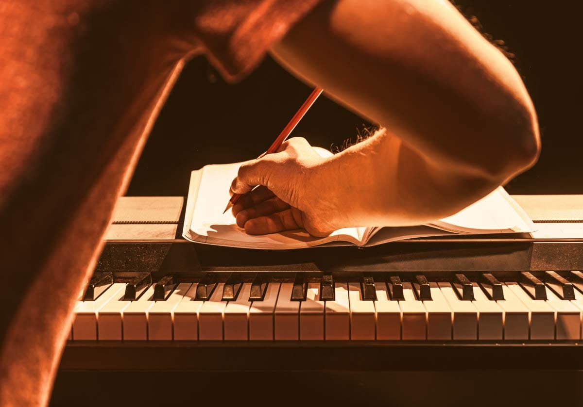Songwriter writing lyrics and musical ideas in a notebook at a piano keyboard
