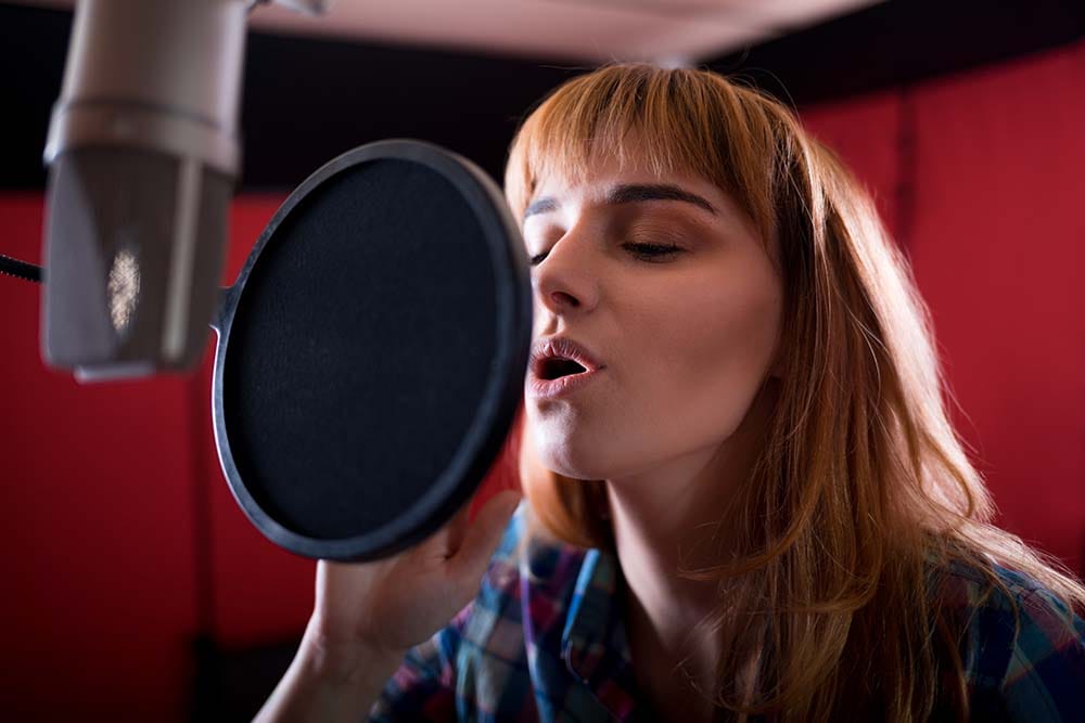 Female vocalist singing into a studio condenser microphone equipped with a pop filter