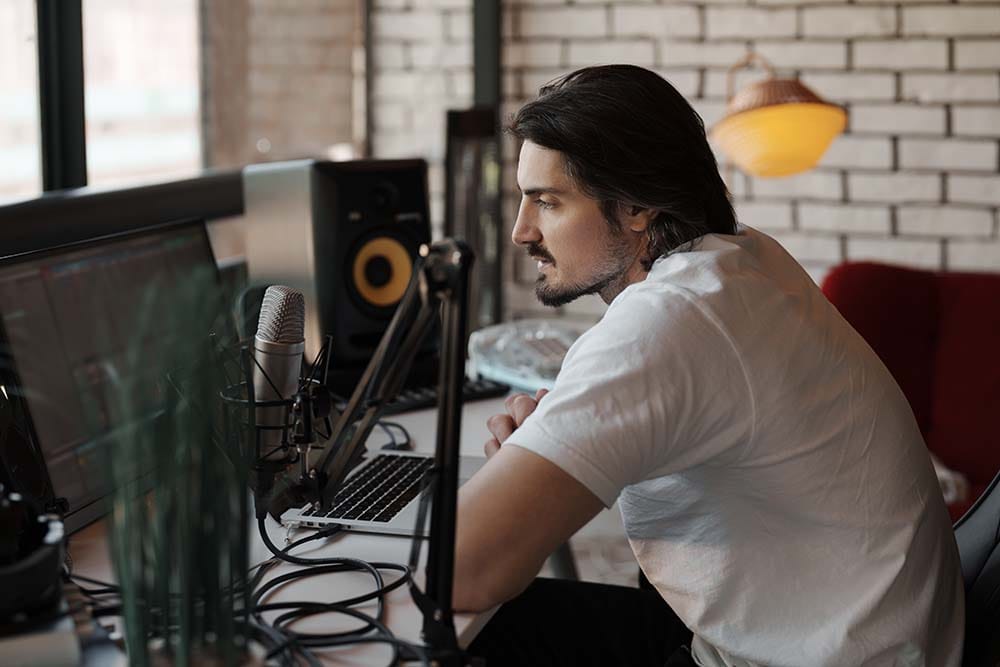 Music producer sitting at a studio desk setting up a DAW template with studio monitors and a microphone setup