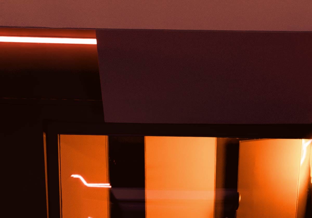 Close-up view of acoustic ceiling clouds and wall treatment panels lit by warm orange LED lights in a home studio