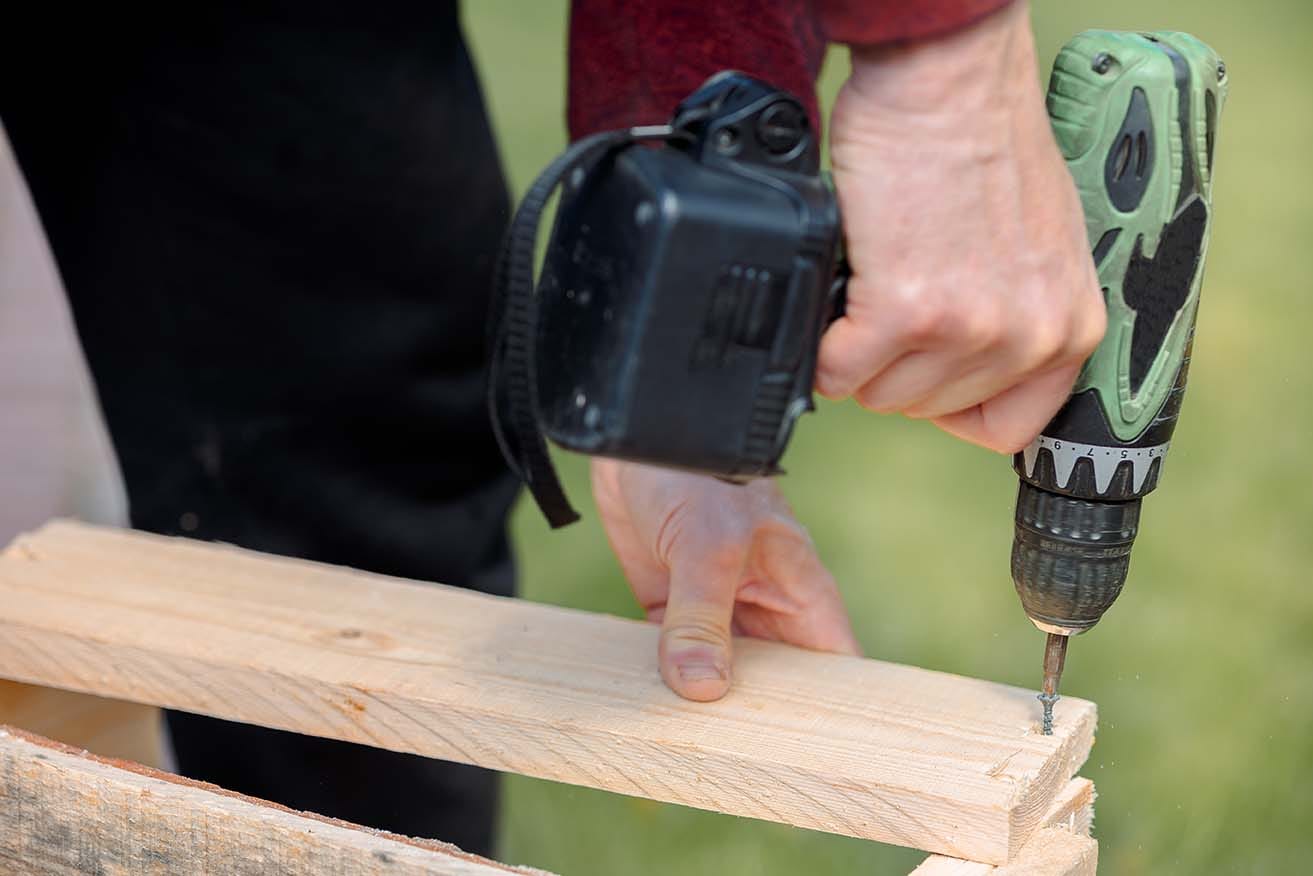 Person using a cordless power drill to drive a screw into a wooden frame for a DIY acoustic panel