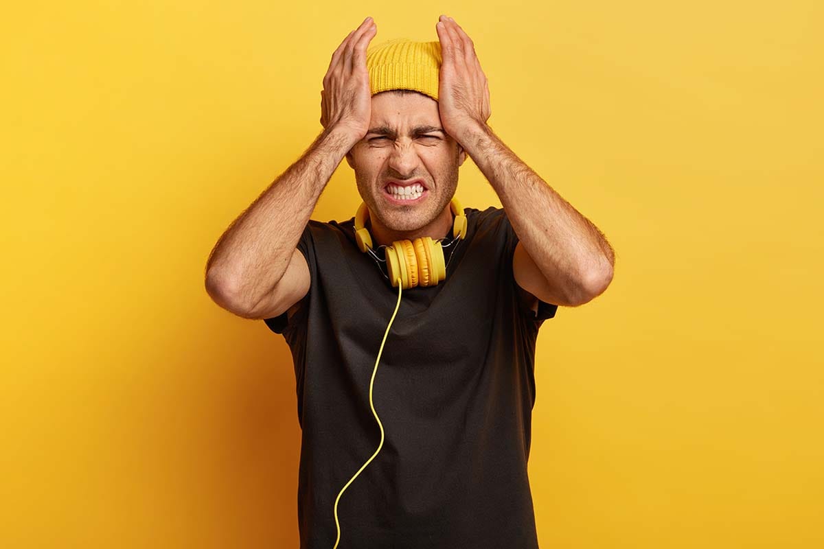 Frustrated music producer wearing headphones and holding his head in an untreated room with bad mix translation