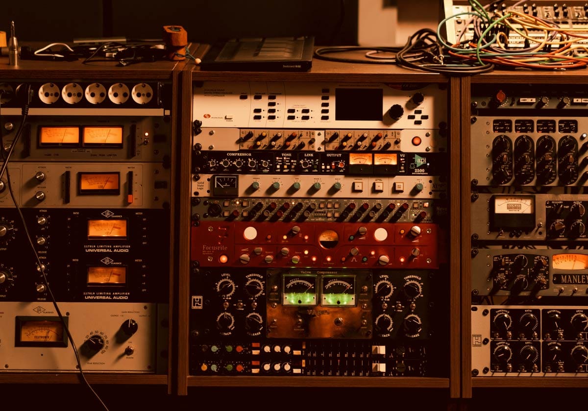Professional rack of analog outboard studio gear with lit VU meters and patch cables in a recording studio