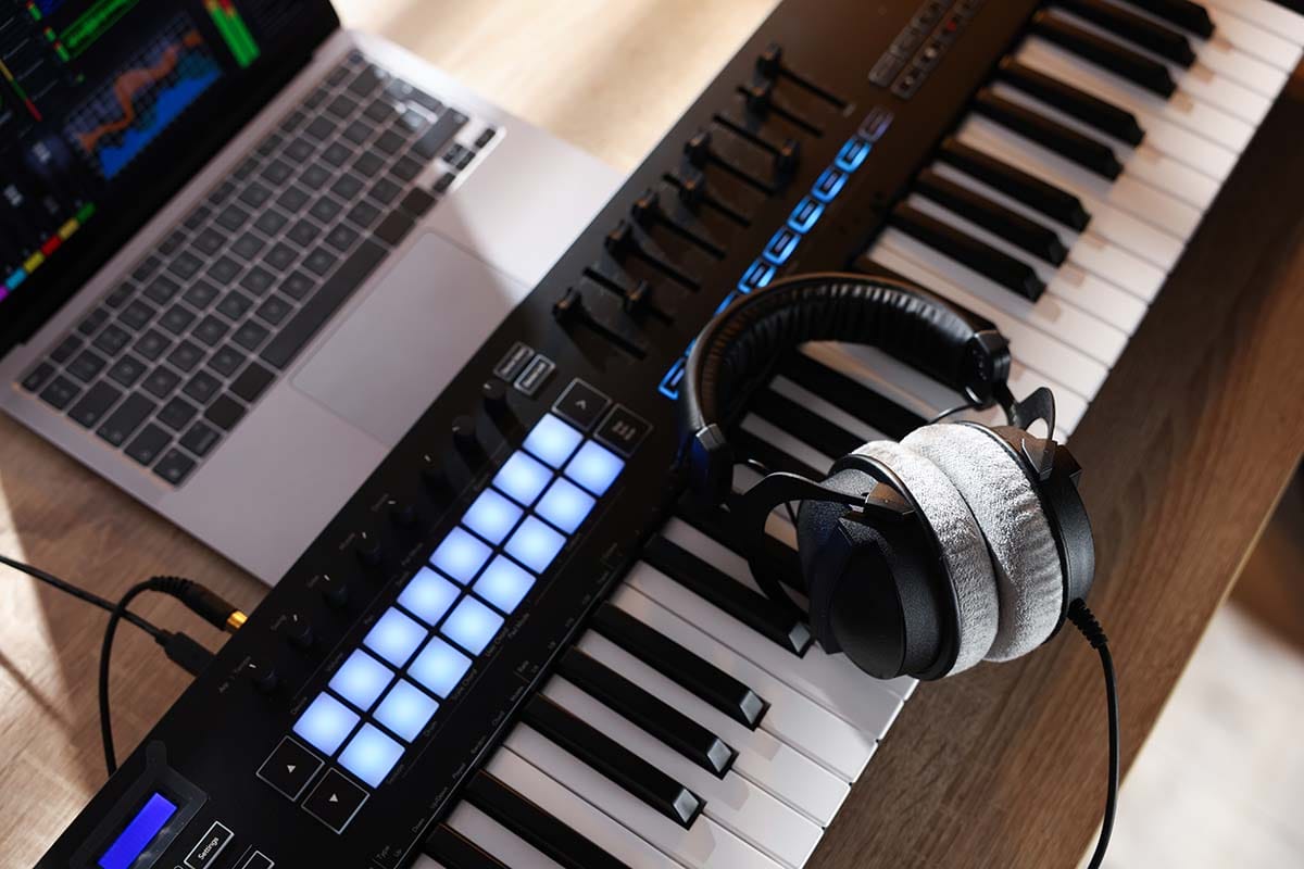 Minimal home studio desk setup featuring a laptop with DAW software, studio headphones, and a MIDI keyboard controller