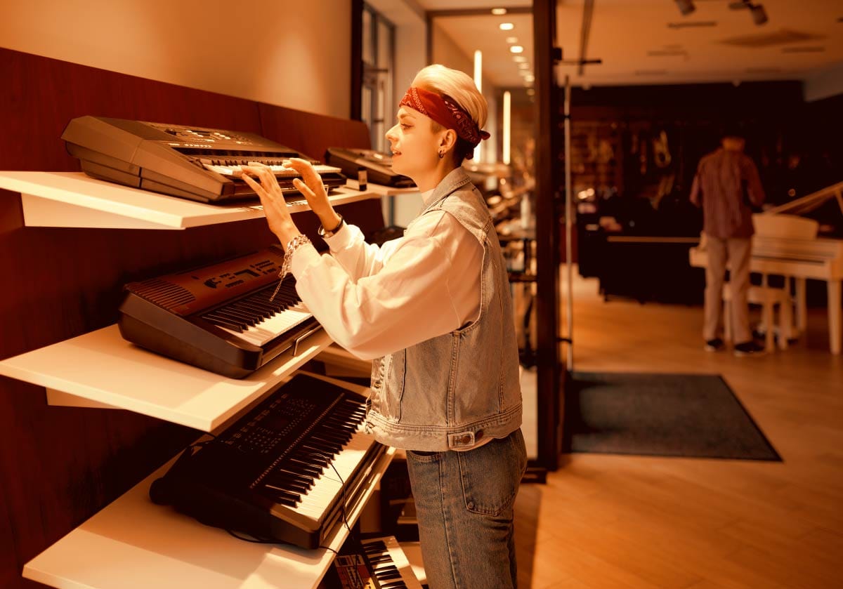 Music producer browsing hardware synthesizers on shelving in a music equipment store