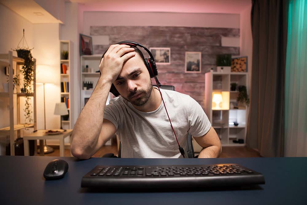 Frustrated music producer resting head in hand at home studio desk in front of computer keyboard