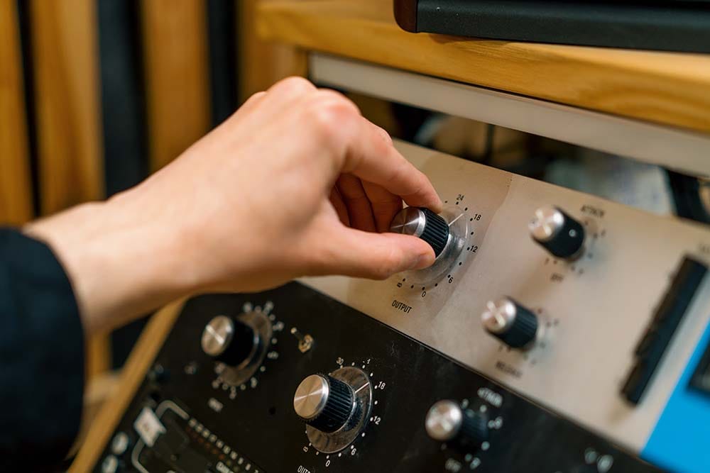 Hand adjusting output gain knob on an outboard analog 1176 limiter compressor rack unit