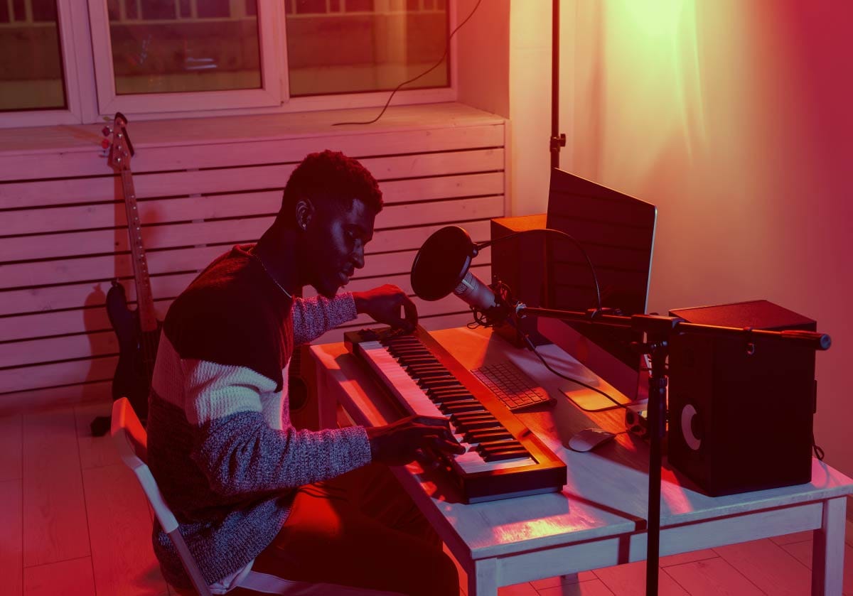 Music producer playing a MIDI keyboard controller at a desk in a home studio setup