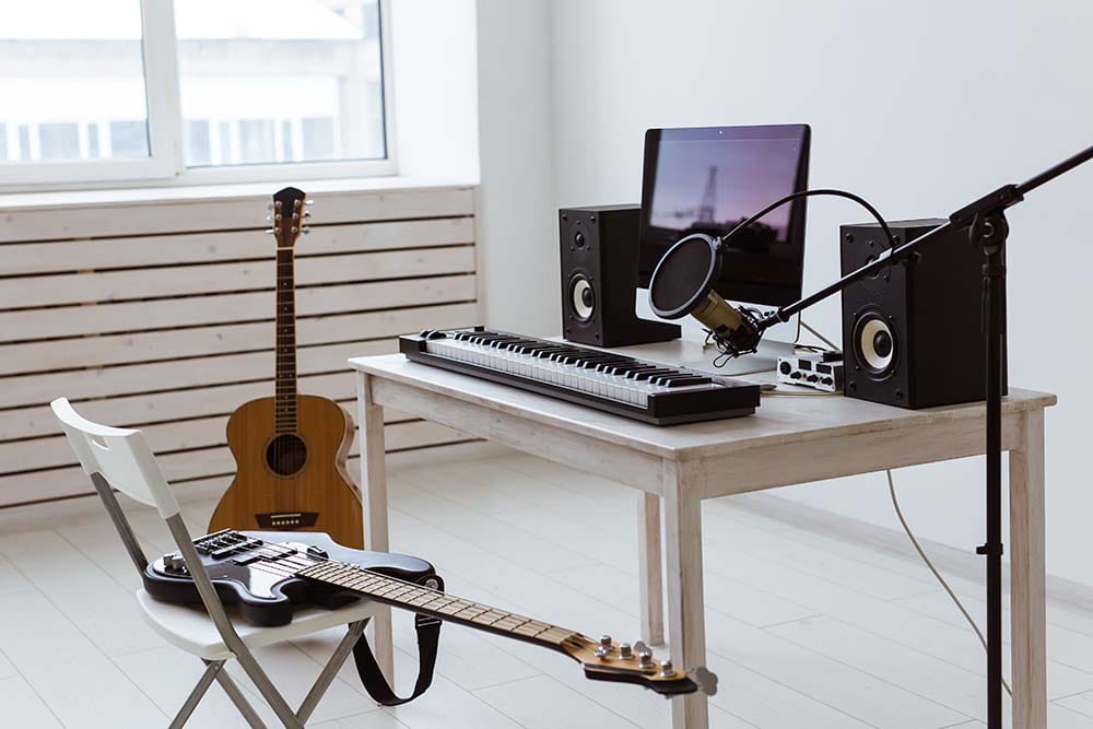 Beginner home recording studio setup with audio interface, condenser microphone, monitors, and guitars