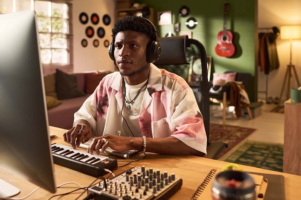 Music producer auditing his DAW templates at a clean home studio computer desk with headphones and a compact MIDI controller