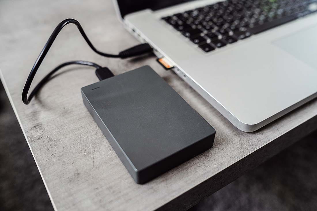 External hard drive plugged into a laptop via USB cable for backing up DAW project files and sample libraries.