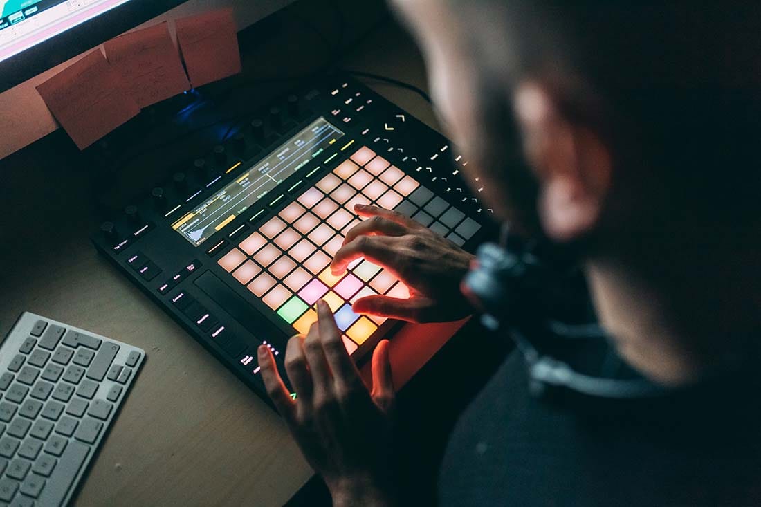 Close-up of a producer tapping illuminated drum pads on a MIDI grid controller during a focused practice session.