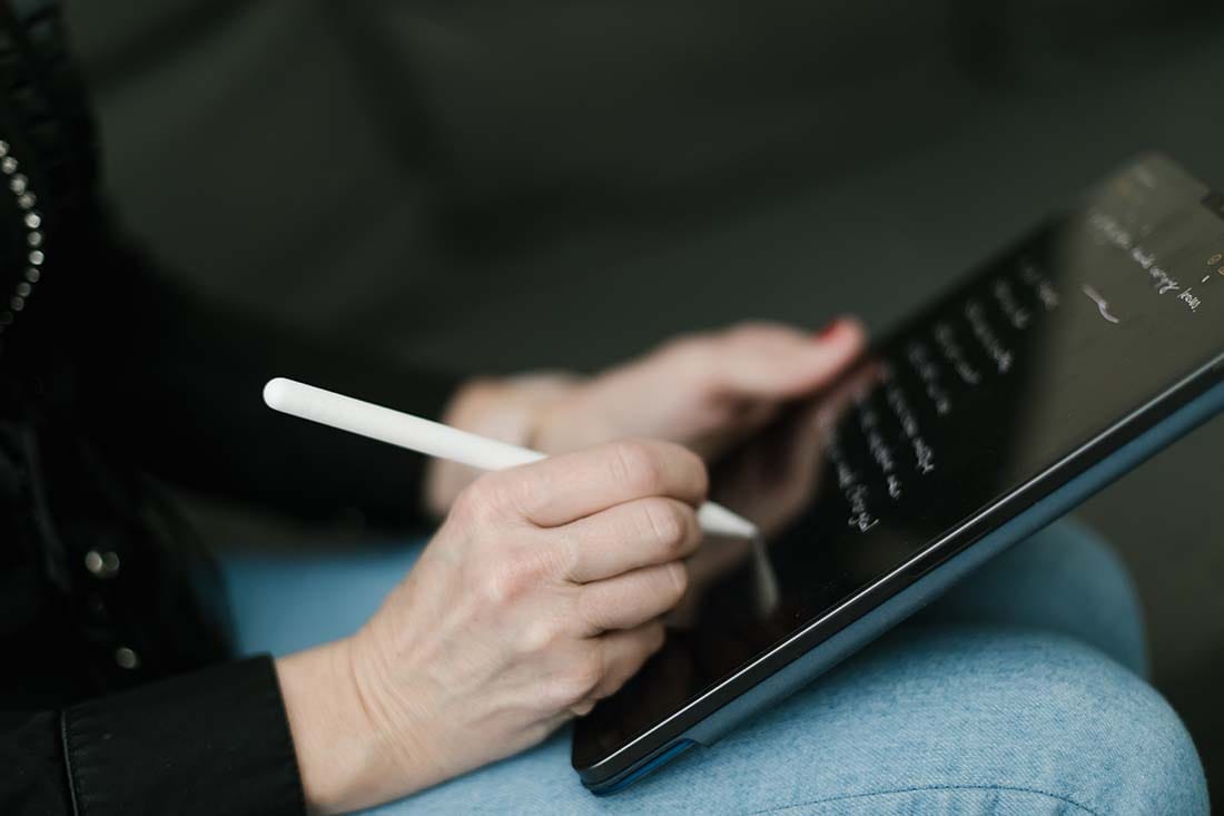 Close-up of someone using a stylus to write handwritten session notes and track progress on a digital tablet.