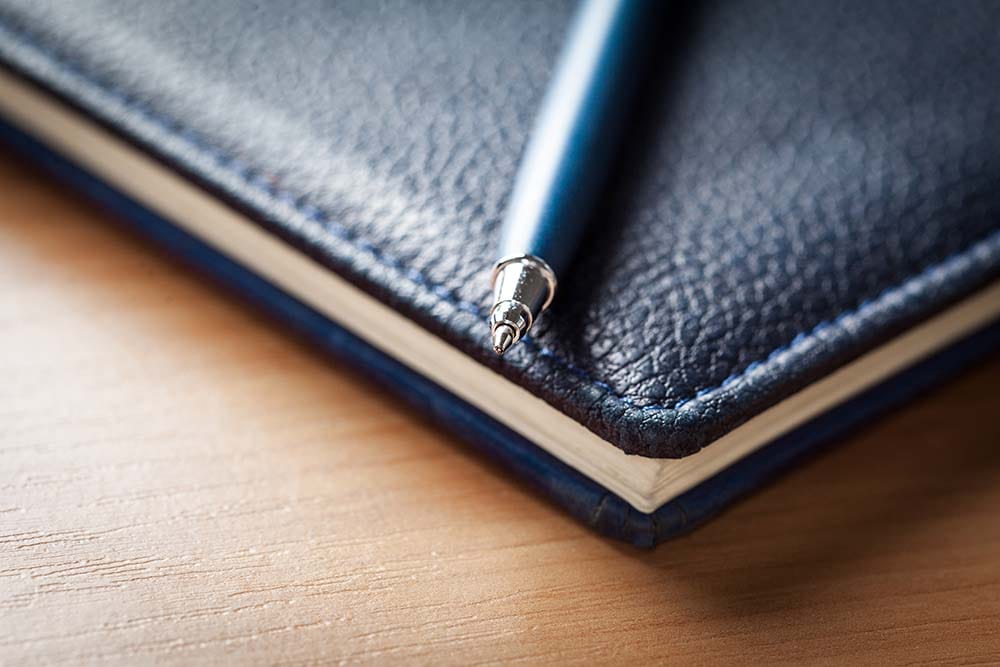 Blue ballpoint pen resting on a dark blue leather journal used for keeping a music production session log.