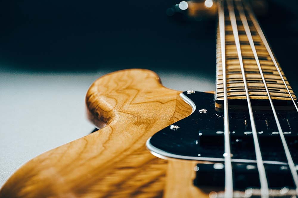 A close-up of a bass guitar with a wood grain body.