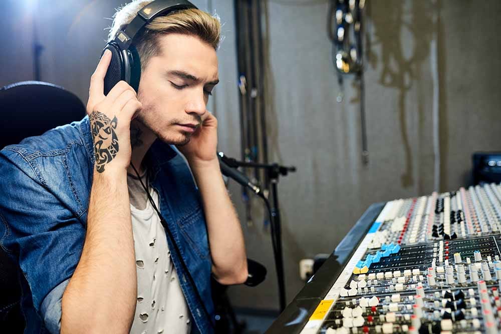 A male producer listens through headphones to an A/B test that is loudness matched for accuracy.